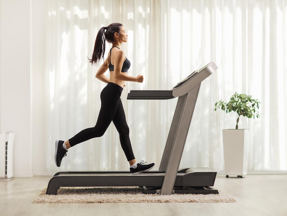 Full length profile shot of a young woman running on a treadmill indoors